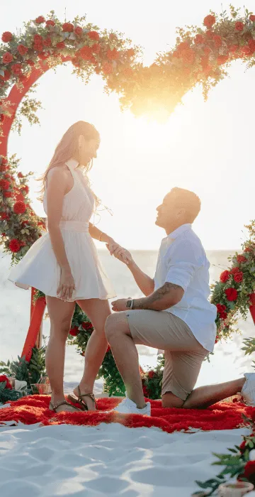 Beach proposal beneath a floral arch